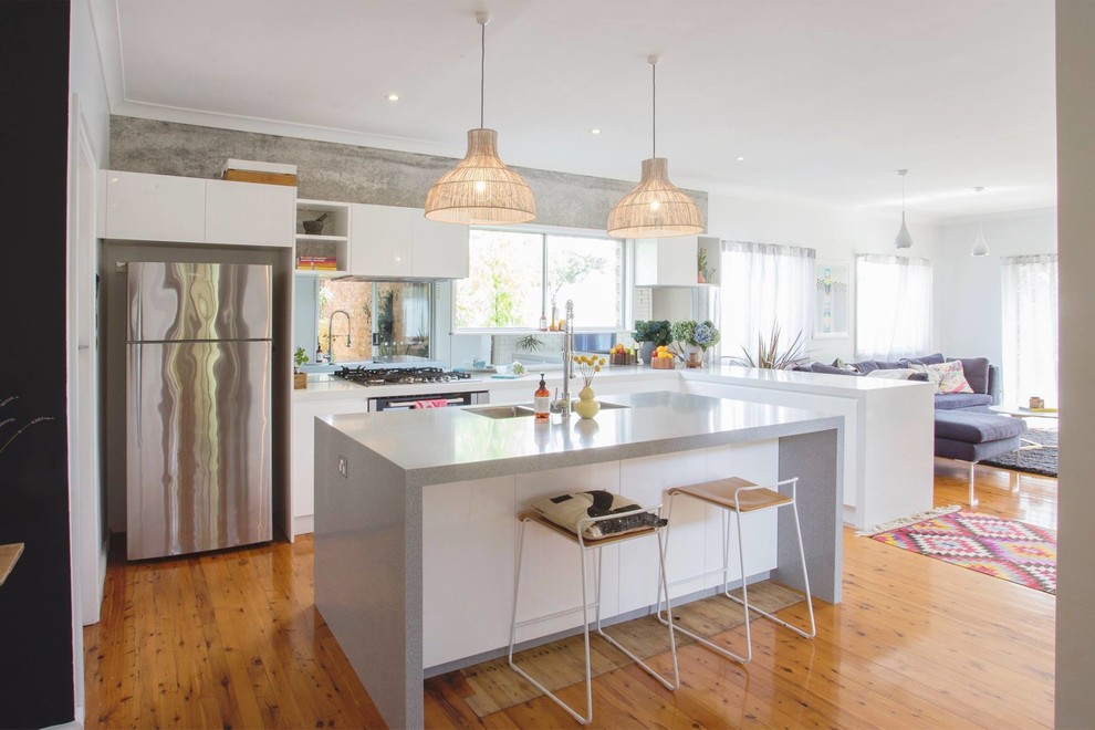 This is an example of a mid-sized modern l-shaped eat-in kitchen in Miami with an undermount sink, flat-panel cabinets, white cabinets, recycled glass benchtops, mirror splashback, stainless steel appliances, medium hardwood floors and with island.