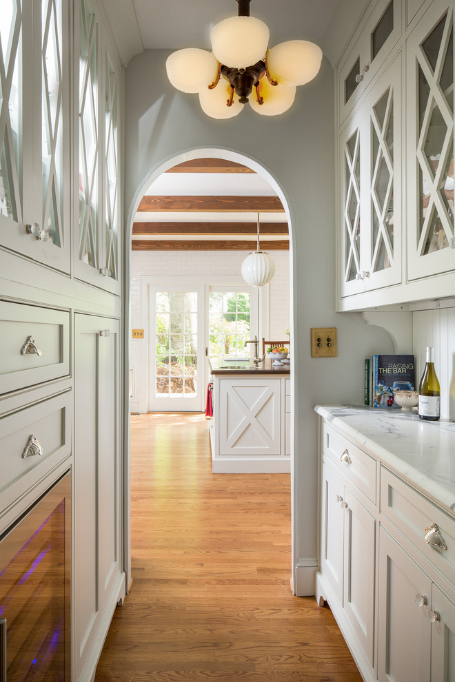 Inspiration for a mid-sized transitional medium tone wood floor and brown floor kitchen pantry remodel in Atlanta with a farmhouse sink, shaker cabinets, white cabinets, marble countertops, white backsplash, subway tile backsplash, stainless steel appliances, an island and white countertops