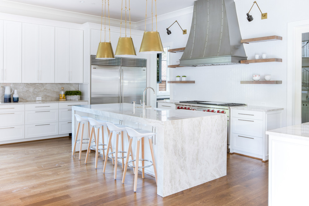 This is an example of a transitional kitchen in Dallas with shaker cabinets, white cabinets, white splashback, stainless steel appliances, medium hardwood floors, with island and beige benchtop.