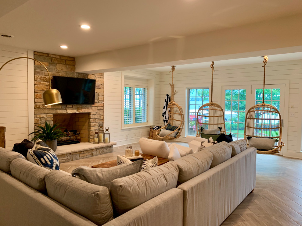 Large transitional walk-out basement in Milwaukee with white walls, porcelain floors, a standard fireplace, a stone fireplace surround and grey floor.