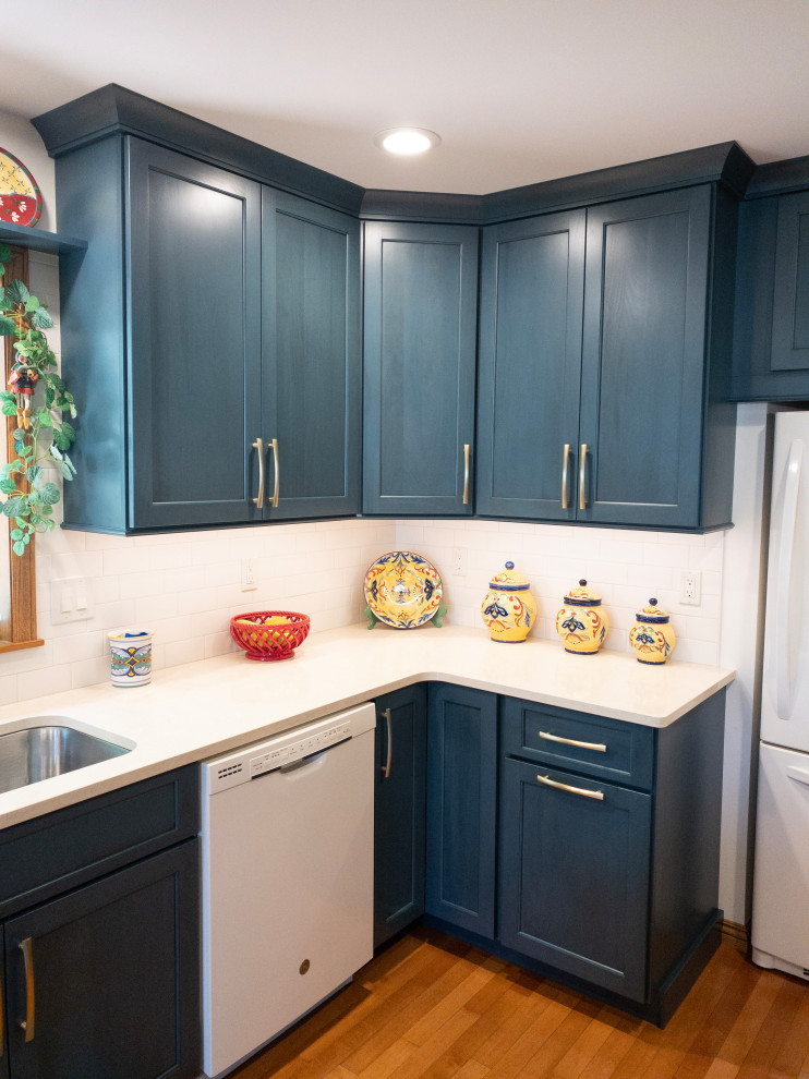 Example of a mid-sized transitional galley light wood floor enclosed kitchen design with an undermount sink, flat-panel cabinets, blue cabinets, quartz countertops, white backsplash, subway tile backsplash, white appliances, a peninsula and white countertops