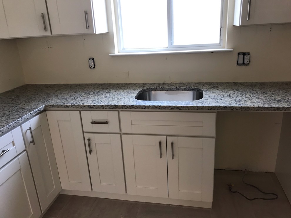 Photo of a small traditional l-shaped separate kitchen in New York with an undermount sink, shaker cabinets, white cabinets, granite benchtops, stainless steel appliances, porcelain floors, grey floor and multi-coloured benchtop.
