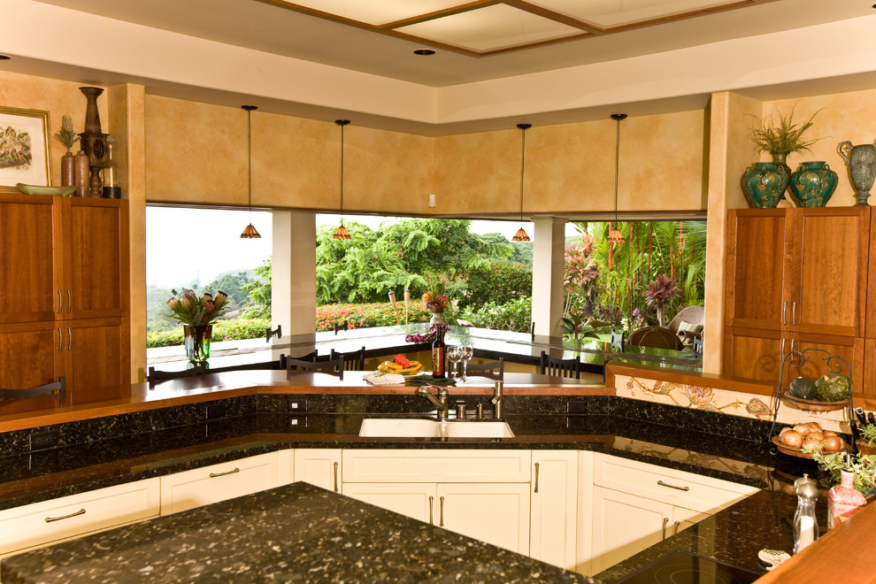 Design ideas for a large tropical u-shaped eat-in kitchen in Hawaii with a double-bowl sink, shaker cabinets, brown cabinets, granite benchtops, beige splashback, stone slab splashback, panelled appliances, concrete floors, multiple islands, brown floor and black benchtop.