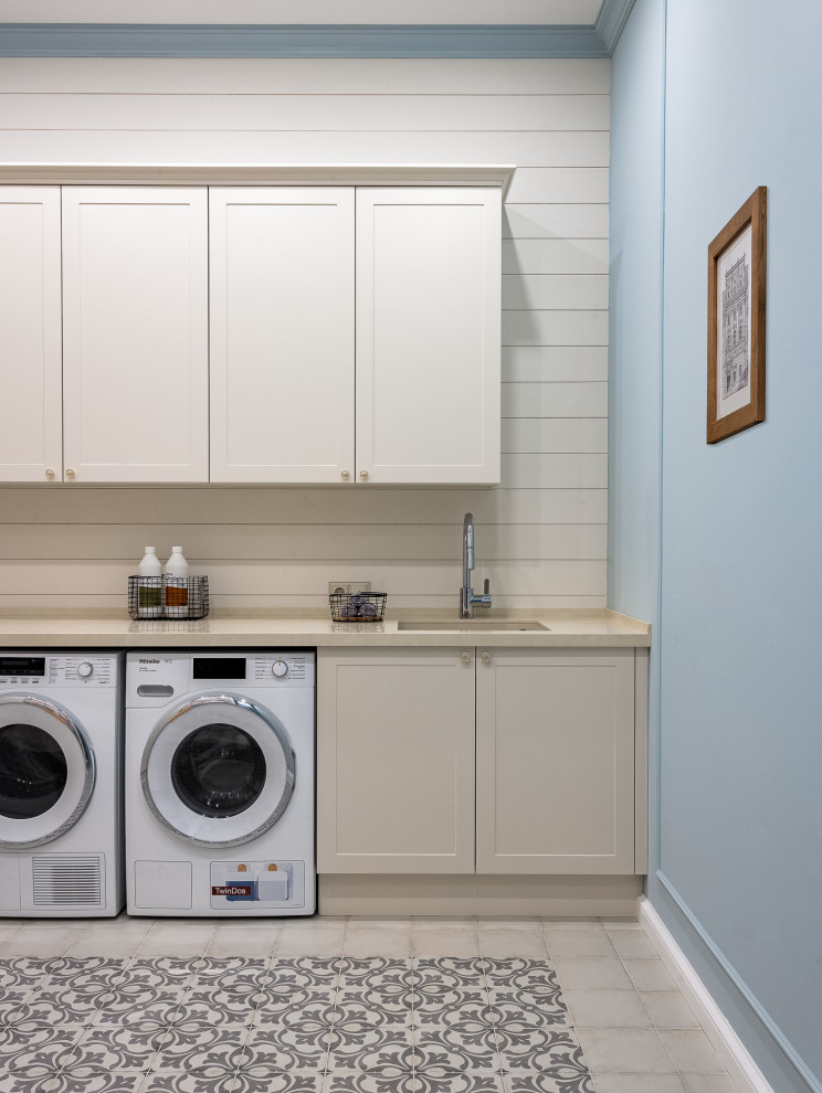 This is an example of a large traditional l-shaped dedicated laundry room in Other with an undermount sink, recessed-panel cabinets, beige cabinets, quartz benchtops, beige splashback, shiplap splashback, blue walls, ceramic floors, a side-by-side washer and dryer, beige floor, beige benchtop and planked wall panelling.