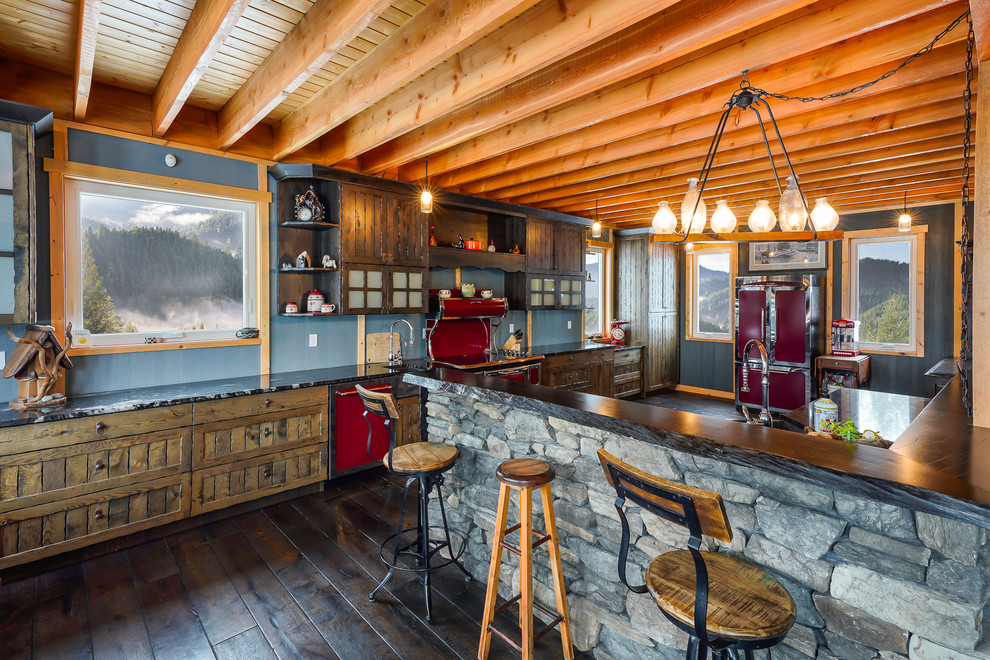 Example of a large mountain style galley eat-in kitchen design with a farmhouse sink, recessed-panel cabinets, brown cabinets, wood countertops, colored appliances and an island