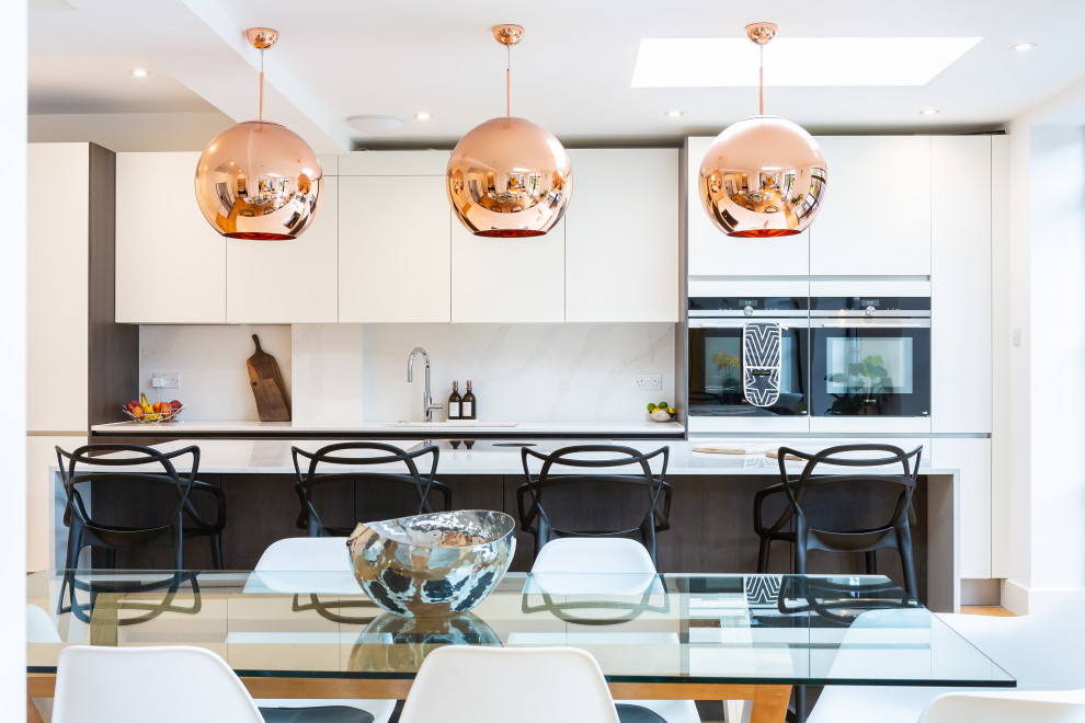 Design ideas for a contemporary galley kitchen in Essex with a submerged sink, flat-panel cabinets, white cabinets, white splashback, stone slab splashback, black appliances, medium hardwood flooring, an island, brown floors and white worktops.