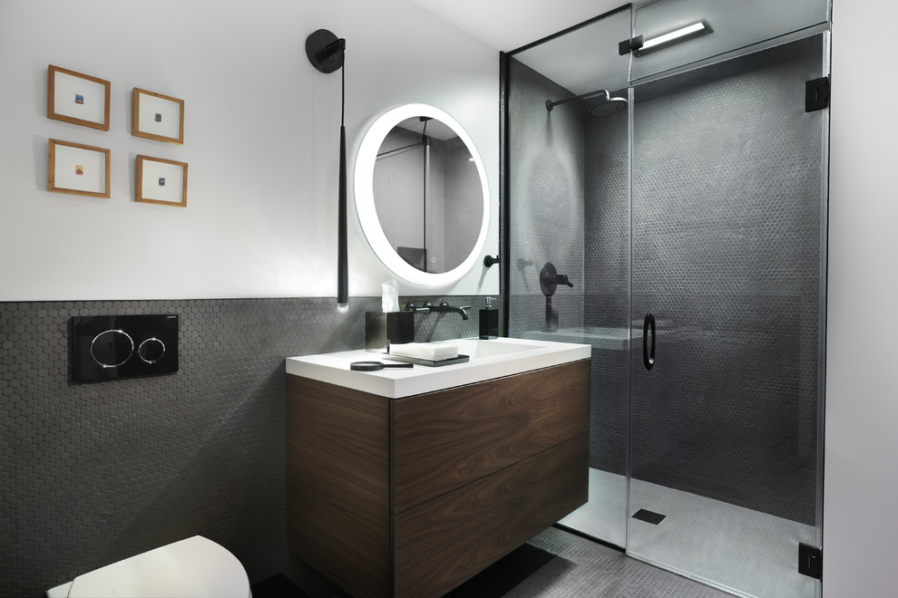 Design ideas for a contemporary 3/4 bathroom in Chicago with flat-panel cabinets, dark wood cabinets, an alcove shower, a wall-mount toilet, black tile, grey walls, an integrated sink, black floor, a hinged shower door and white benchtops.