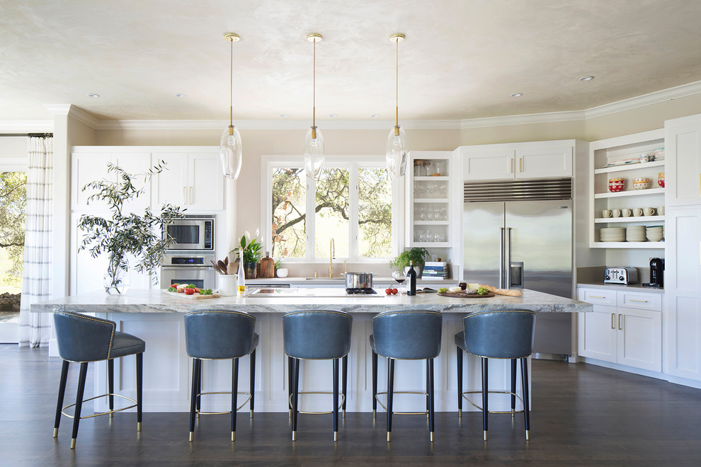 This is an example of a contemporary kitchen in Orange County with a single-bowl sink, recessed-panel cabinets, white cabinets, marble benchtops, beige splashback, limestone splashback, stainless steel appliances, dark hardwood floors, with island, grey floor and blue benchtop.