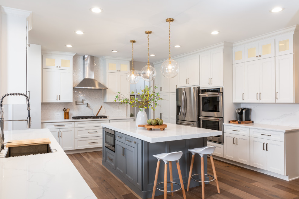 Inspiration for a classic u-shaped kitchen in DC Metro with a submerged sink, recessed-panel cabinets, white cabinets, white splashback, stainless steel appliances, medium hardwood flooring, an island, brown floors and white worktops.