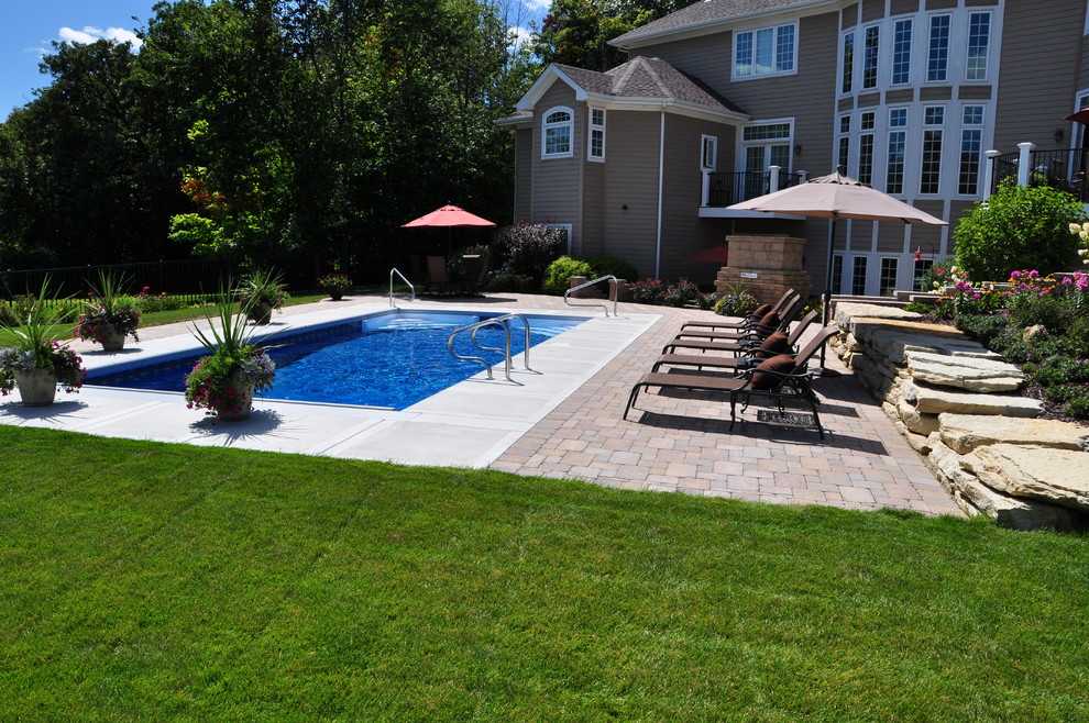This is an example of an expansive traditional backyard rectangular pool in Chicago with brick pavers.