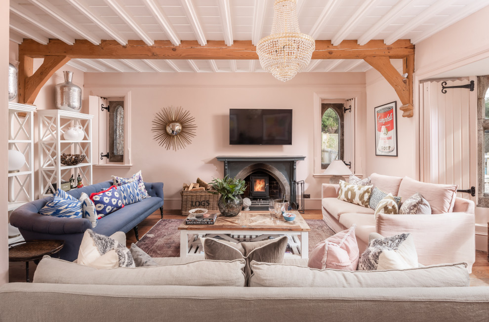 Inspiration pour un grand salon traditionnel fermé avec un mur rose, un sol en bois brun, une cheminée standard, un manteau de cheminée en pierre et poutres apparentes.