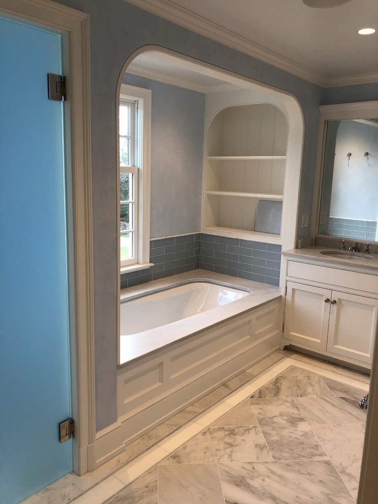 Mid-sized traditional master bathroom in New York with beaded inset cabinets, white cabinets, an undermount tub, an alcove shower, a two-piece toilet, black and white tile, marble, blue walls, marble floors, an undermount sink, marble benchtops, grey floor, a hinged shower door and white benchtops.