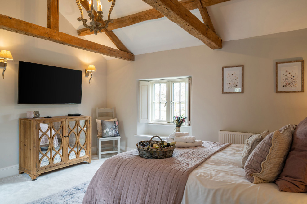 Photo of a large rural master and grey and pink bedroom in Gloucestershire with pink walls, carpet, beige floors and exposed beams.