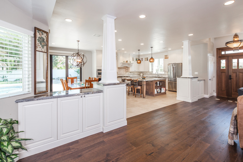 Inspiration for a mid-sized arts and crafts l-shaped eat-in kitchen in San Diego with an undermount sink, shaker cabinets, white cabinets, granite benchtops, white splashback, stone tile splashback, stainless steel appliances, limestone floors and with island.