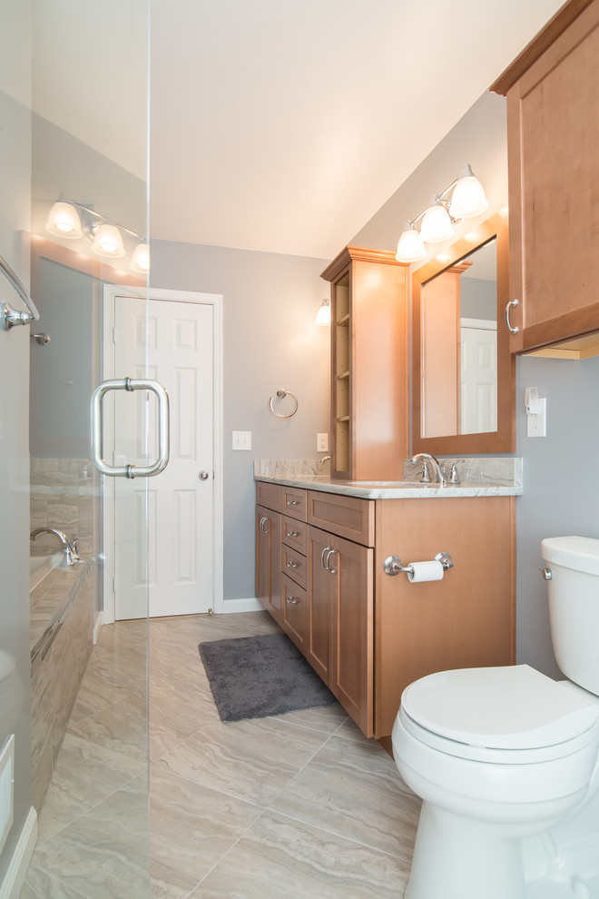 Photo of a mid-sized traditional master bathroom in DC Metro with an undermount sink, recessed-panel cabinets, medium wood cabinets, granite benchtops, a drop-in tub, an alcove shower, a two-piece toilet, beige tile, porcelain tile, blue walls, porcelain floors, grey floor and a hinged shower door.