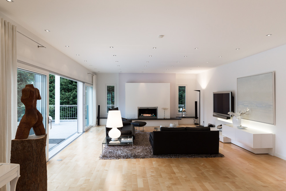 Inspiration for an expansive contemporary formal living room in Frankfurt with white walls, light hardwood floors, a standard fireplace, a plaster fireplace surround and a wall-mounted tv.