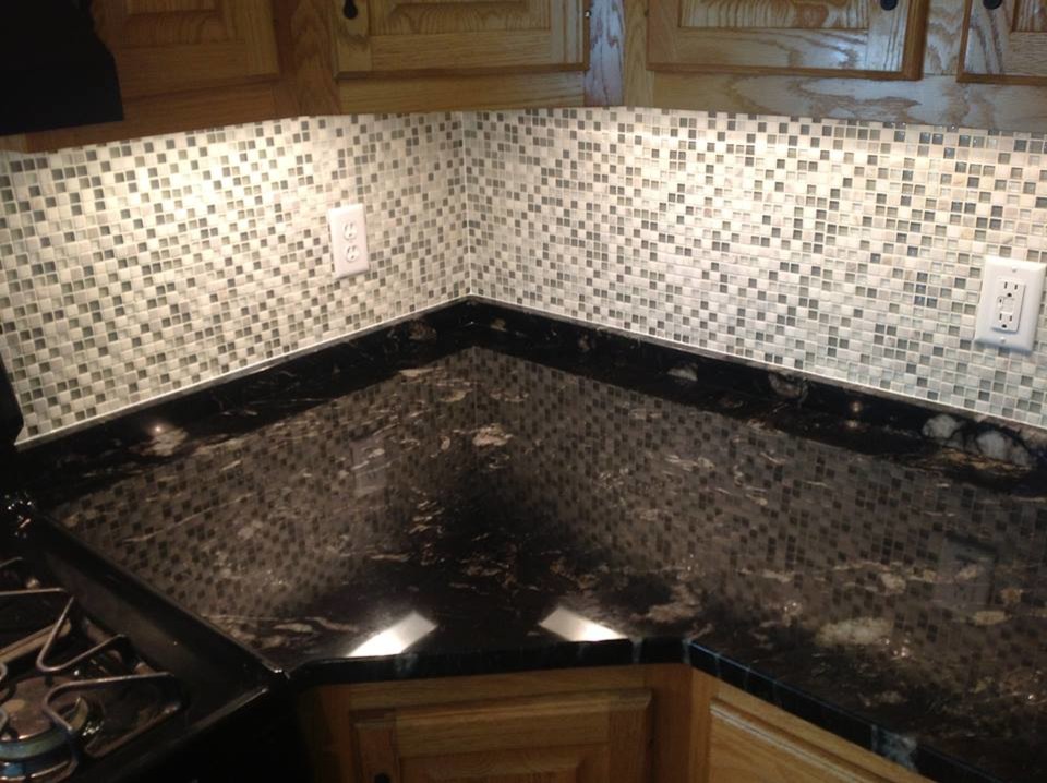 Example of a l-shaped open concept kitchen design with recessed-panel cabinets, light wood cabinets, marble countertops, multicolored backsplash, mirror backsplash and black appliances