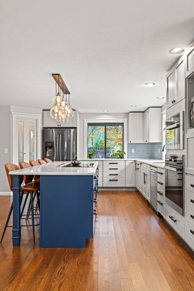 Klassische Küche in L-Form mit Unterbauwaschbecken, Schrankfronten im Shaker-Stil, grauen Schränken, Küchenrückwand in Blau, Küchengeräten aus Edelstahl, braunem Holzboden, Kücheninsel, braunem Boden und weißer Arbeitsplatte in Denver