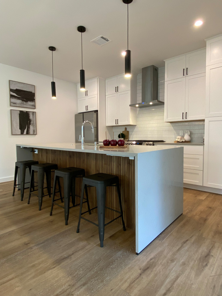 Inspiration for a galley open concept kitchen remodel in Austin with an undermount sink, shaker cabinets, white cabinets, quartz countertops, white backsplash, ceramic backsplash, stainless steel appliances, an island and gray countertops