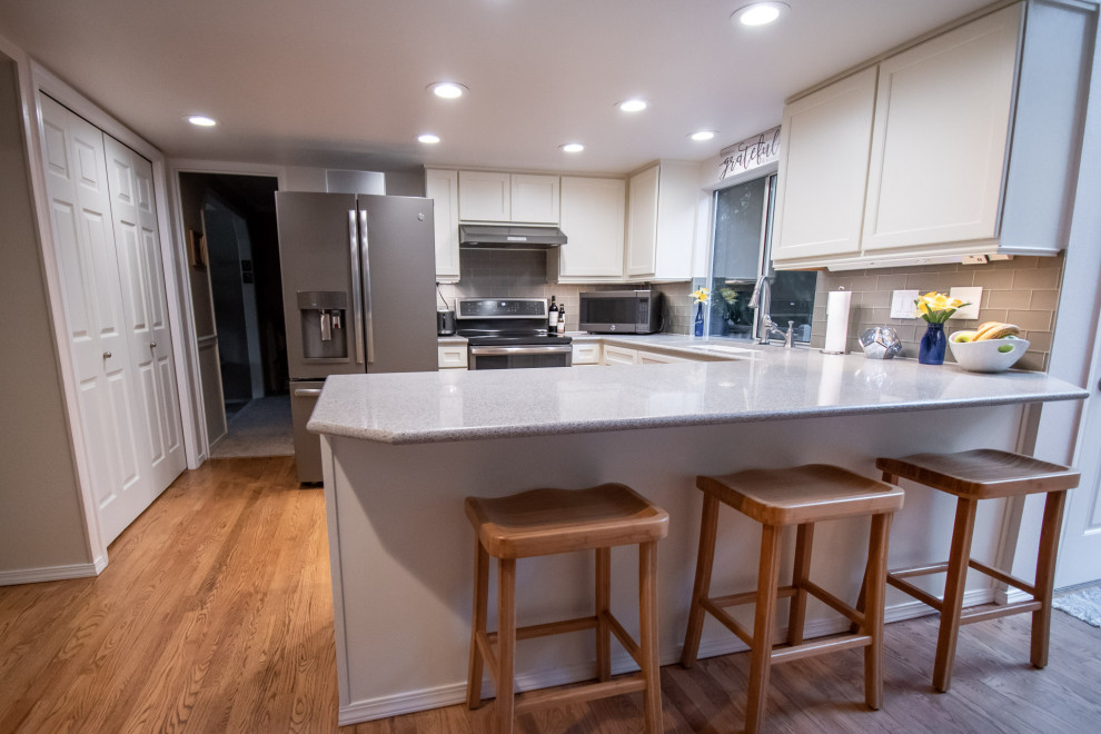 Example of a transitional u-shaped medium tone wood floor open concept kitchen design in Seattle with an undermount sink, shaker cabinets, white cabinets, quartz countertops, gray backsplash, glass tile backsplash, stainless steel appliances, a peninsula and multicolored countertops