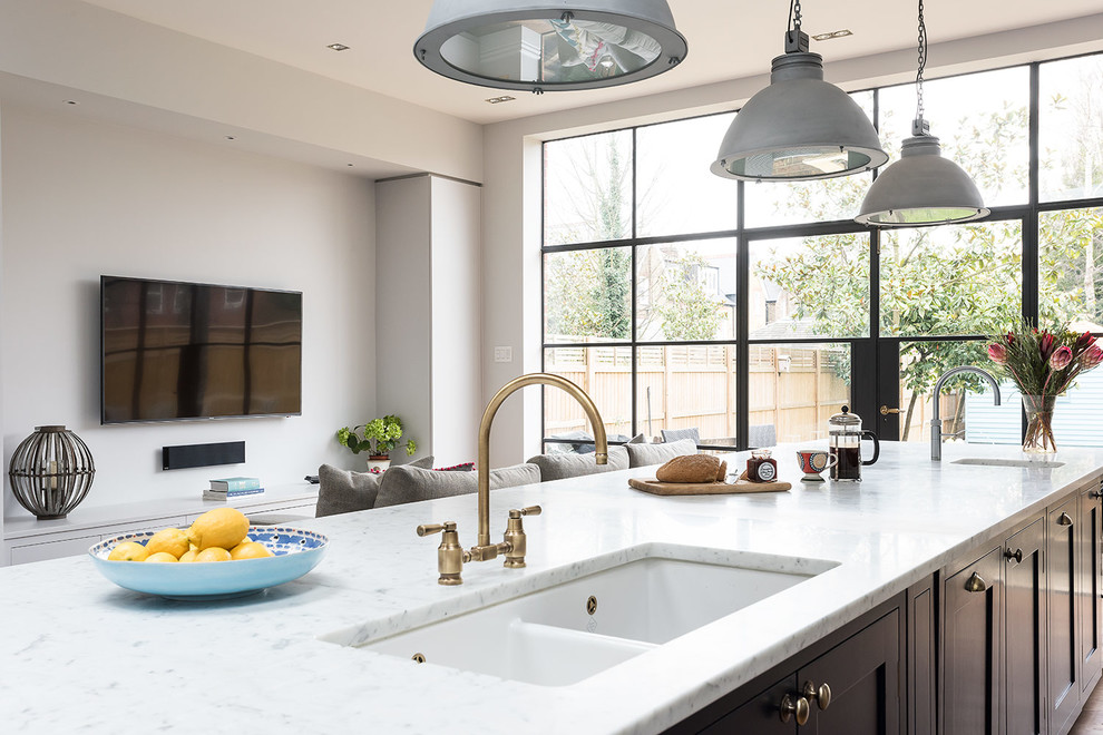 Photo of a large traditional u-shaped kitchen/diner with a belfast sink, shaker cabinets, blue cabinets, marble worktops, metallic splashback, glass tiled splashback, integrated appliances, medium hardwood flooring and an island.