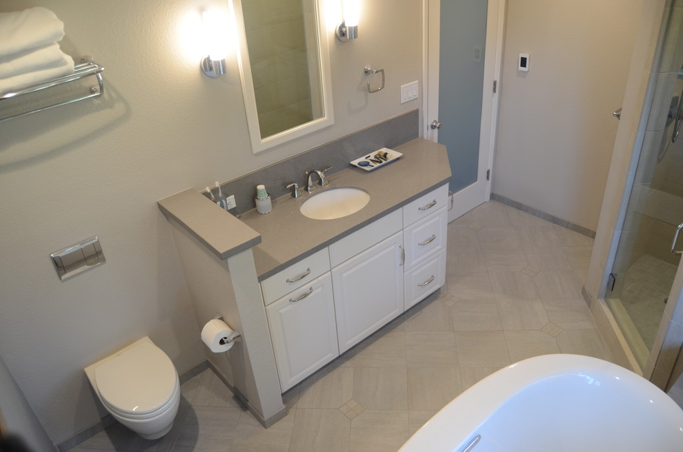 Transitional bathroom in San Francisco with raised-panel cabinets, white cabinets, a freestanding tub, a corner shower, a wall-mount toilet, beige tile, porcelain tile, grey walls, porcelain floors, an undermount sink and engineered quartz benchtops.