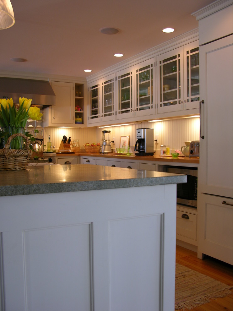 This is an example of a small traditional l-shaped open plan kitchen in Boston with a farmhouse sink, glass-front cabinets, white cabinets, wood benchtops, white splashback, panelled appliances, medium hardwood floors and with island.