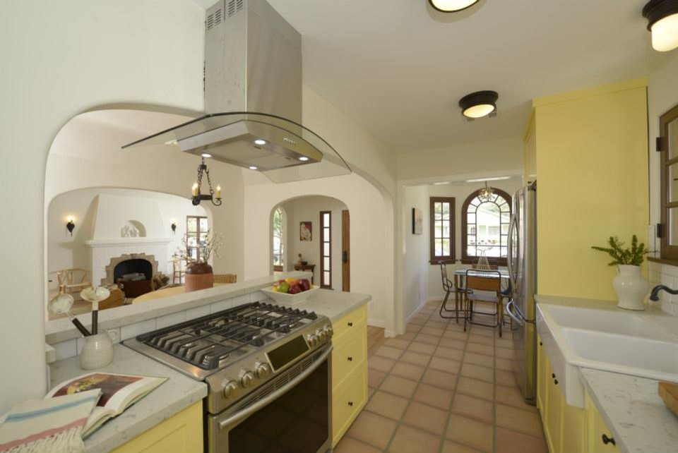 This is an example of a mid-sized galley eat-in kitchen in Los Angeles with a double-bowl sink, shaker cabinets, yellow cabinets, white splashback, ceramic splashback, stainless steel appliances, terra-cotta floors and no island.