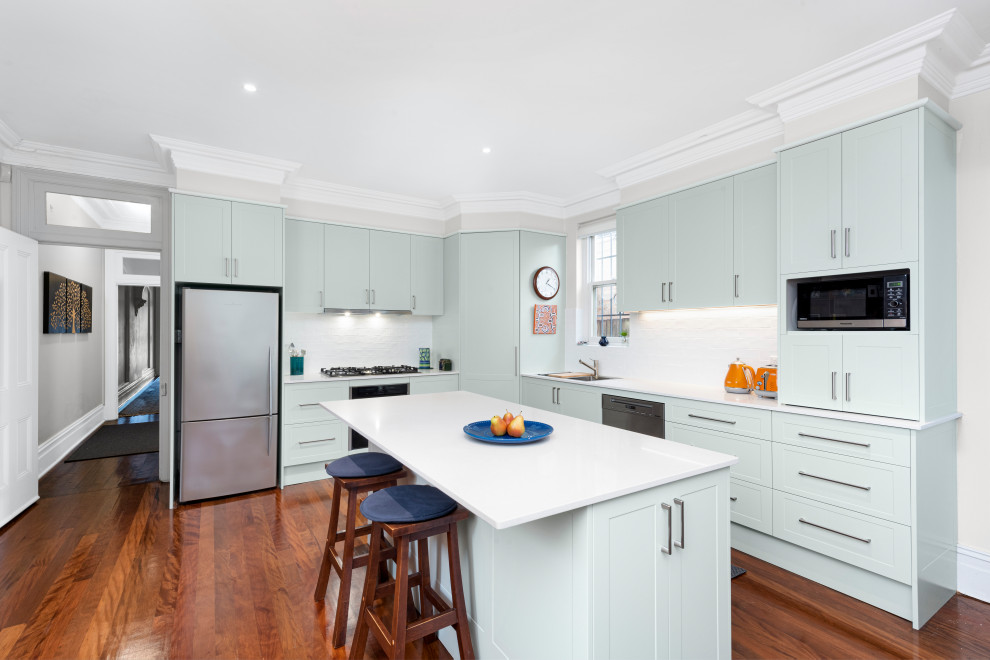 This is an example of a mid-sized modern l-shaped kitchen pantry in Sydney with blue cabinets, quartz benchtops, white splashback, ceramic splashback, stainless steel appliances, with island and white benchtop.