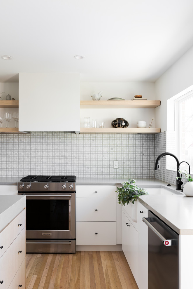 Inspiration for a small scandinavian l-shaped kitchen/diner in Salt Lake City with a belfast sink, flat-panel cabinets, light wood cabinets, engineered stone countertops, grey splashback, mosaic tiled splashback, stainless steel appliances, light hardwood flooring, an island, beige floors and grey worktops.