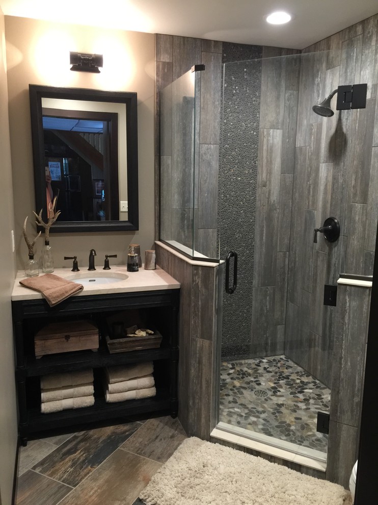 Photo of a small country 3/4 bathroom in Other with an undermount sink, dark wood cabinets, engineered quartz benchtops, a corner shower, gray tile, pebble tile, beige walls, ceramic floors and open cabinets.