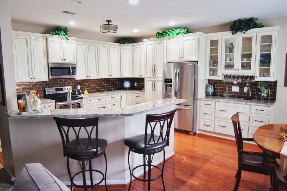 Kitchen - mid-sized u-shaped medium tone wood floor and brown floor kitchen idea in Charleston with an undermount sink, raised-panel cabinets, beige cabinets, granite countertops, brown backsplash, ceramic backsplash, stainless steel appliances and beige countertops