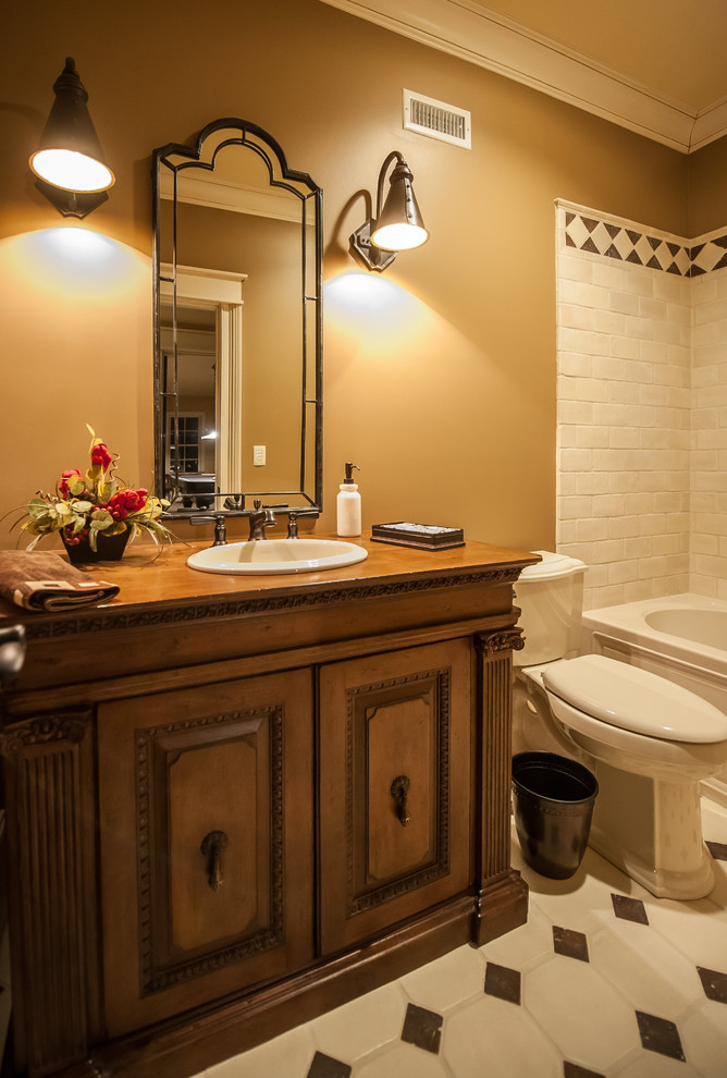 Photo of a mid-sized country bathroom in Louisville with a drop-in sink, raised-panel cabinets, distressed cabinets, a drop-in tub, a shower/bathtub combo, a one-piece toilet, multi-coloured tile and brown walls.