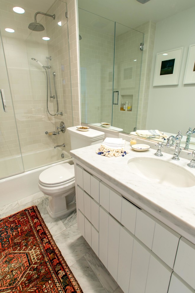 Photo of a mid-sized beach style bathroom in Other with an undermount sink, flat-panel cabinets, white cabinets, a shower/bathtub combo, white walls, marble floors, a two-piece toilet, white tile, porcelain tile and marble benchtops.