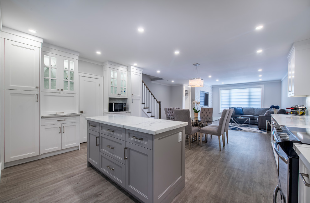 Mid-sized transitional u-shaped eat-in kitchen in Toronto with an undermount sink, recessed-panel cabinets, white cabinets, quartzite benchtops, multi-coloured splashback, mosaic tile splashback, stainless steel appliances, light hardwood floors, with island, grey floor and white benchtop.