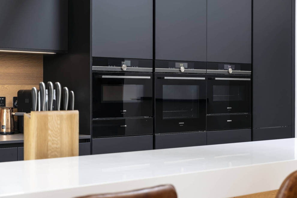 Inspiration för mellanstora moderna linjära flerfärgat kök med öppen planlösning, med en dubbel diskho, släta luckor, svarta skåp, bänkskiva i kvartsit, brunt stänkskydd, stänkskydd i trä, svarta vitvaror, en köksö och svart golv