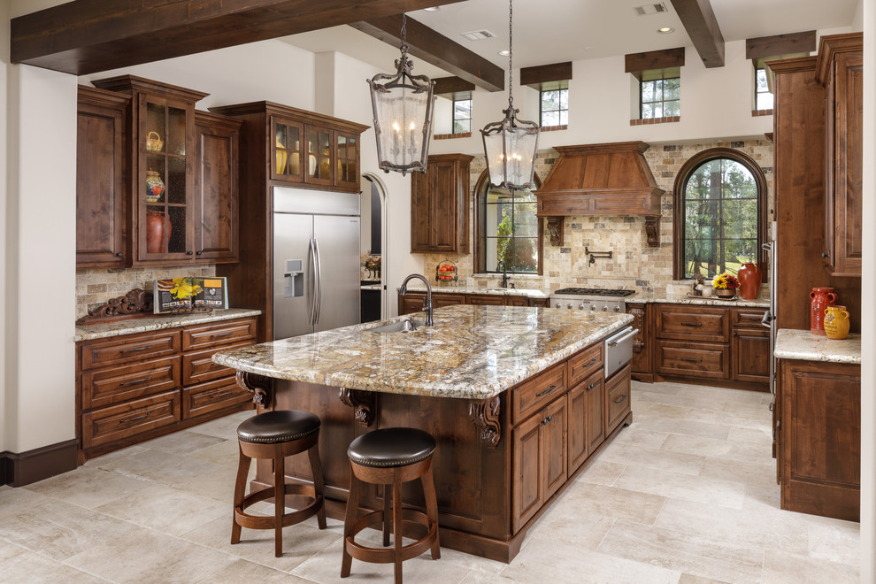 This is an example of a large mediterranean u-shaped eat-in kitchen in Houston with a drop-in sink, raised-panel cabinets, dark wood cabinets, limestone benchtops, black splashback, stainless steel appliances, porcelain floors, with island, beige floor and beige benchtop.