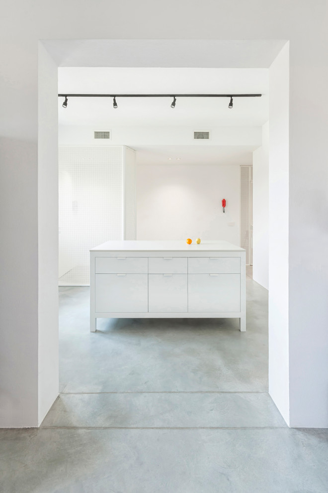Modelo de cocina lineal actual pequeña cerrada con puertas de armario blancas, encimera de cuarcita, suelo de cemento, una isla, suelo gris y encimeras blancas