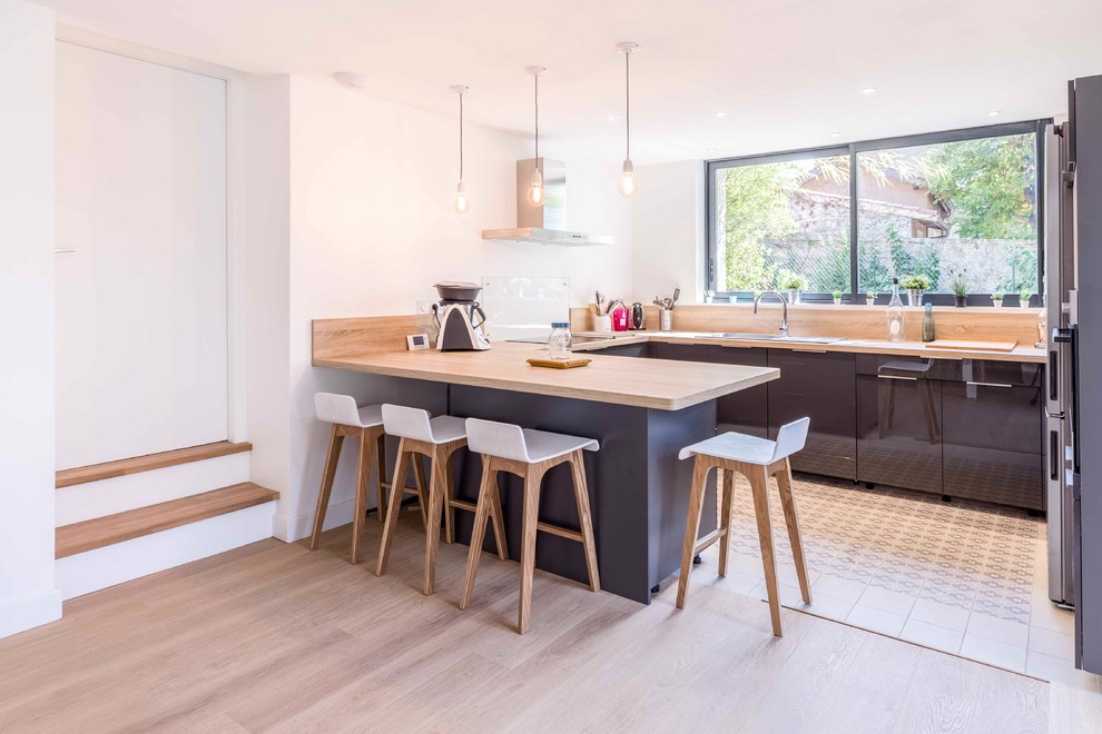 Contemporary u-shaped open plan kitchen in Lyon with a drop-in sink, flat-panel cabinets, grey cabinets, wood benchtops, stainless steel appliances, a peninsula and beige floor.