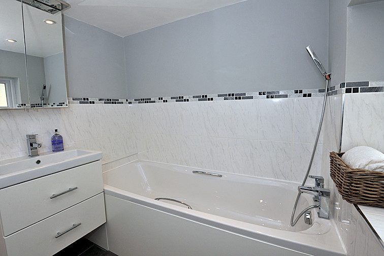 This is an example of a small country kids bathroom in Hertfordshire with flat-panel cabinets, white cabinets, a drop-in tub, a shower/bathtub combo, a two-piece toilet, gray tile, ceramic tile, grey walls, porcelain floors and a wall-mount sink.