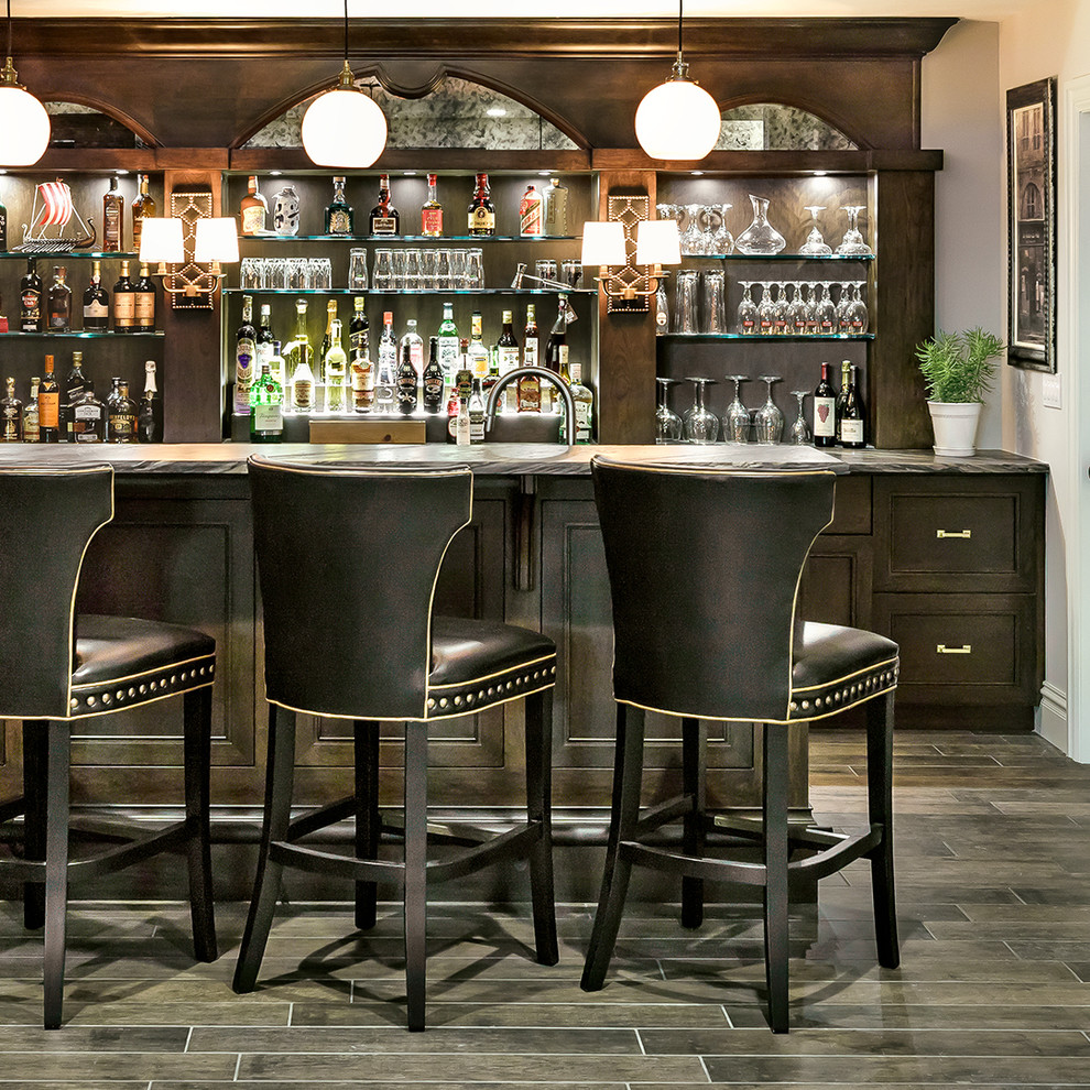 Inspiration for a large transitional seated home bar in Chicago with dark wood cabinets, granite benchtops, ceramic floors, recessed-panel cabinets and grey floor.
