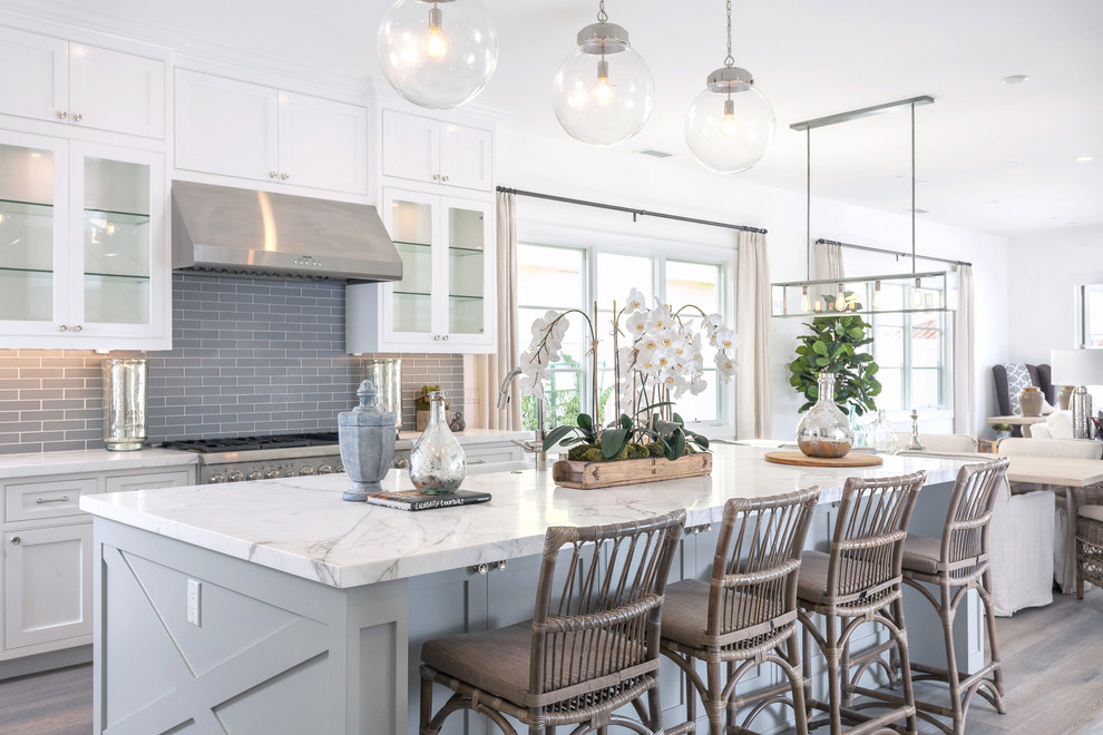 Design ideas for a beach style kitchen in Orange County with marble benchtops, grey splashback, with island, beaded inset cabinets, white cabinets, subway tile splashback, stainless steel appliances and dark hardwood floors.