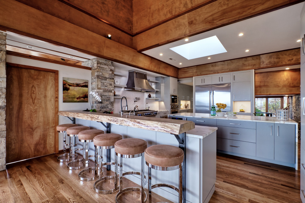 Design ideas for a rustic u-shaped kitchen in Other with flat-panel cabinets, grey cabinets, white splashback, stainless steel appliances, medium hardwood flooring, an island, brown floors and white worktops.