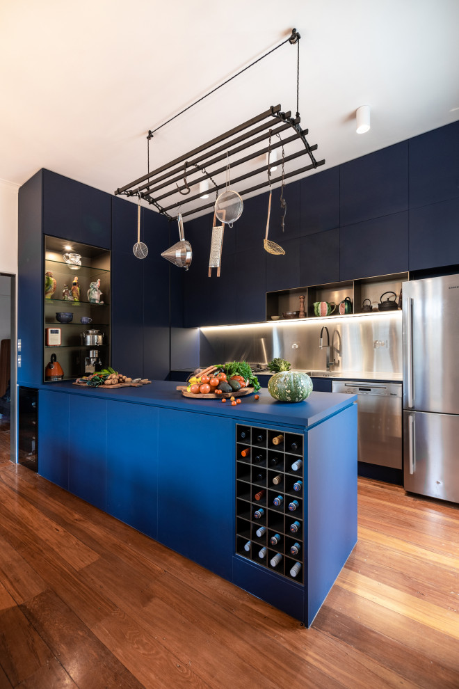 This is an example of a large contemporary u-shaped kitchen in Hobart with a double-bowl sink, flat-panel cabinets, blue cabinets, solid surface benchtops, grey splashback, stainless steel appliances, medium hardwood floors, a peninsula, brown floor and blue benchtop.