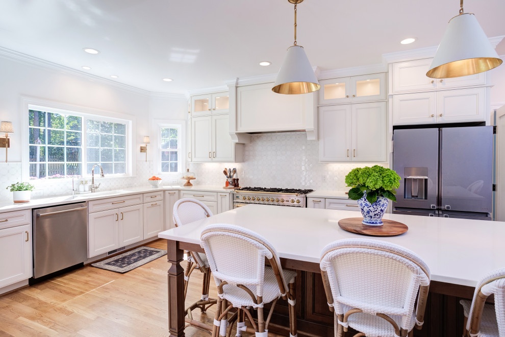 Photo of a large traditional l-shaped open plan kitchen in Raleigh with a submerged sink, recessed-panel cabinets, white cabinets, engineered stone countertops, white splashback, porcelain splashback, stainless steel appliances, medium hardwood flooring, an island, brown floors and white worktops.
