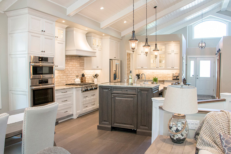 Large transitional l-shaped eat-in kitchen photo with a double-bowl sink, shaker cabinets, white cabinets, beige backsplash, stainless steel appliances and an island