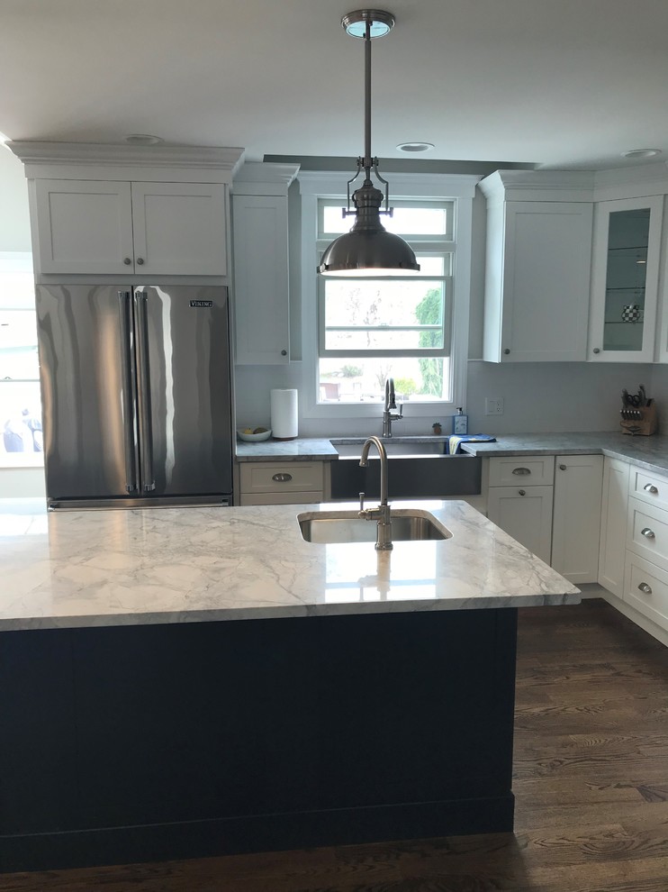 Example of a mid-sized transitional u-shaped dark wood floor and brown floor eat-in kitchen design in New York with a farmhouse sink, recessed-panel cabinets, white cabinets, wood countertops, white backsplash, limestone backsplash, stainless steel appliances, an island and white countertops