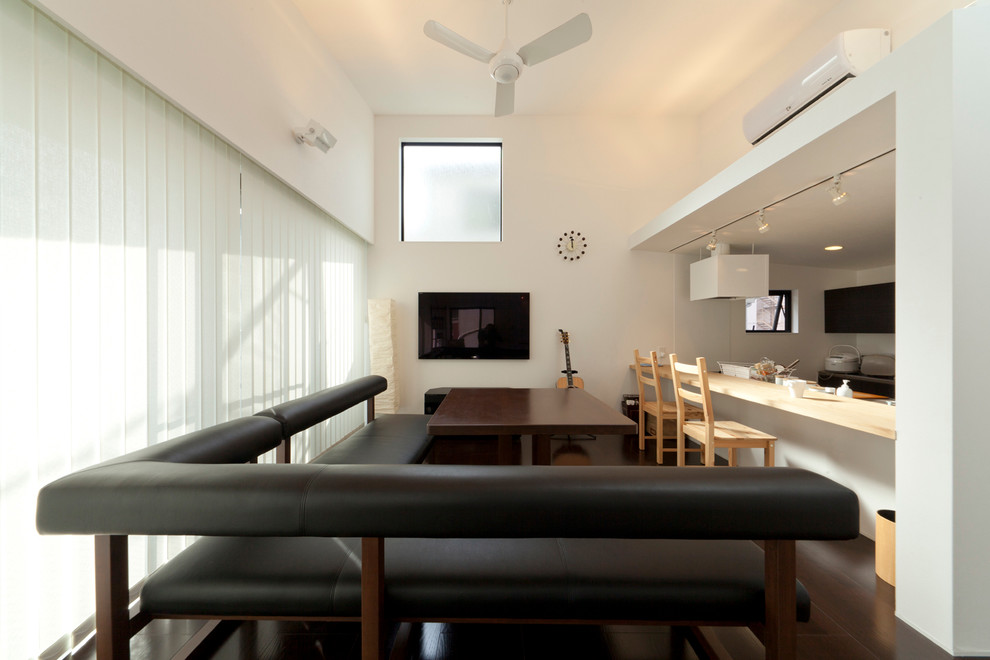 This is an example of an asian open concept living room in Tokyo with white walls, dark hardwood floors, no fireplace, a wall-mounted tv and brown floor.