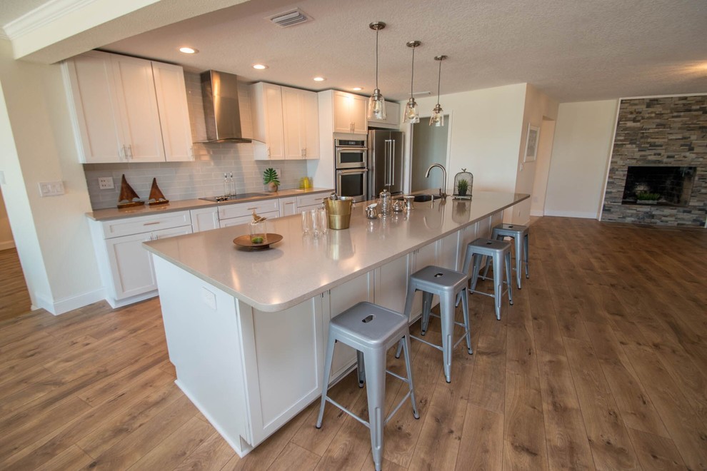 Inspiration for a large beach style galley open plan kitchen in Tampa with an undermount sink, shaker cabinets, white cabinets, quartz benchtops, grey splashback, glass tile splashback, stainless steel appliances, medium hardwood floors and with island.