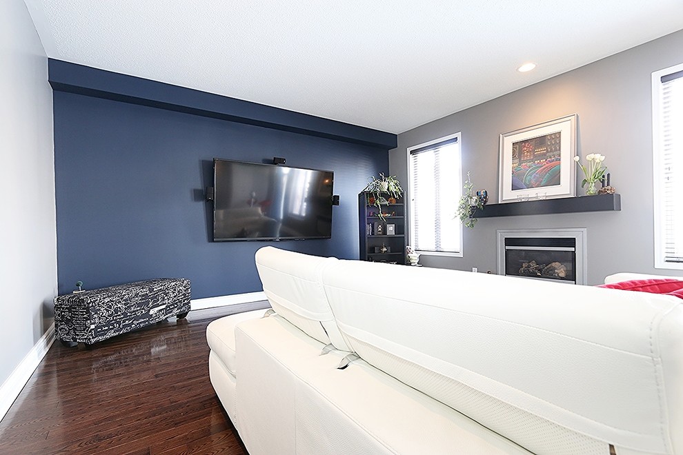 Design ideas for a mid-sized modern enclosed family room in Ottawa with blue walls, dark hardwood floors, a wall-mounted tv and a standard fireplace.